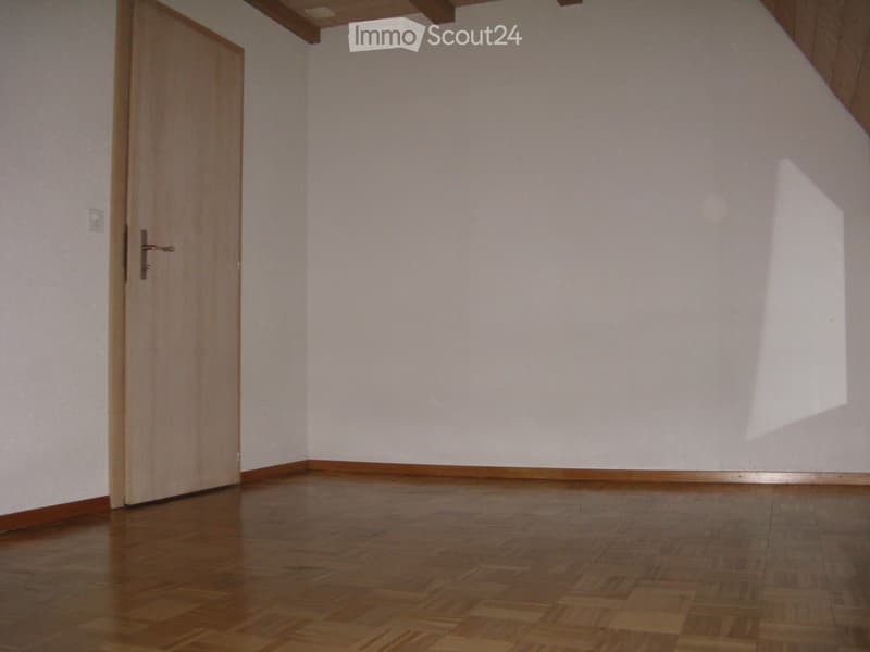 Empty room with wooden flooring, white walls, and a single wooden door.