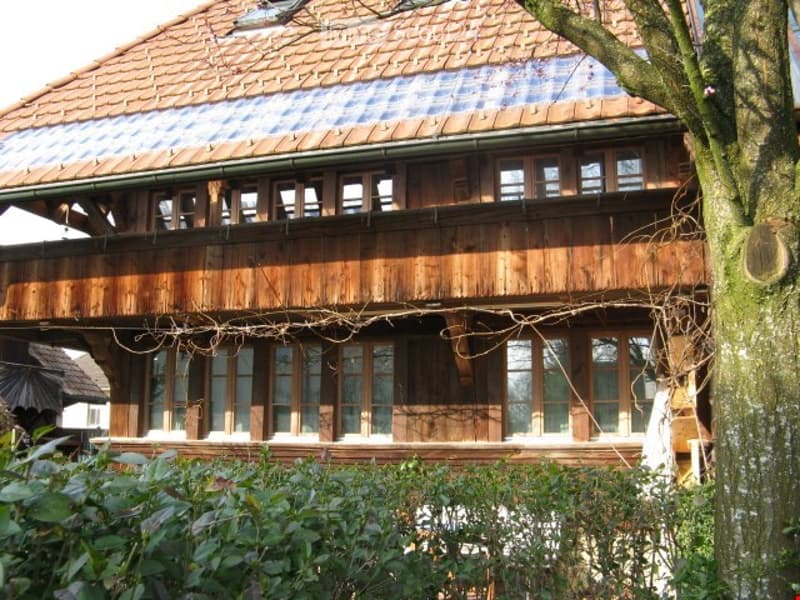 Traditional wooden house with a tiled roof, large windows, and a balcony on the upper floor.