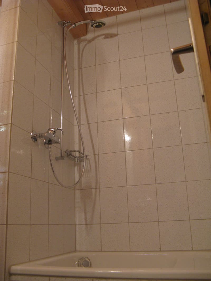 Bathroom with a bathtub, showerhead, and faucet. Light-colored tiled walls and a wooden ceiling.