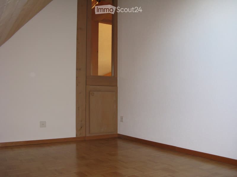 Empty room with wooden flooring, white walls, and a wooden door leading to another room.