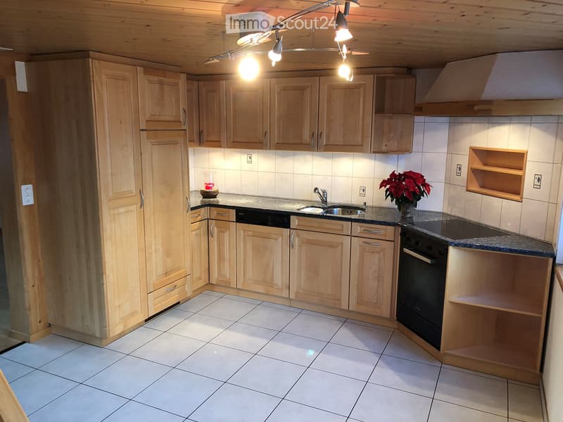 Bright kitchen with light wooden cabinets, white tiled walls, and a granite countertop. Features include a sink, faucet, oven, and a decorative flower pot on the counter.