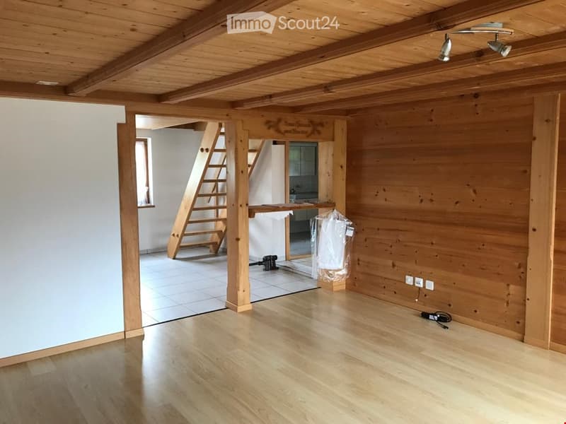 Empty room with wooden flooring, white tiled area, wooden staircase leading to another level, and exposed wooden beams on the ceiling.