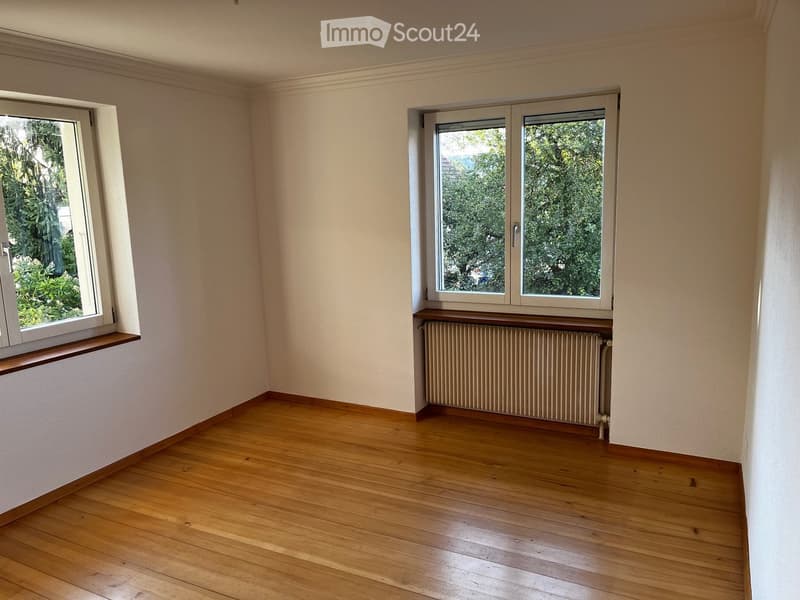 Empty room with wooden flooring, white walls, and two windows with radiators below them.