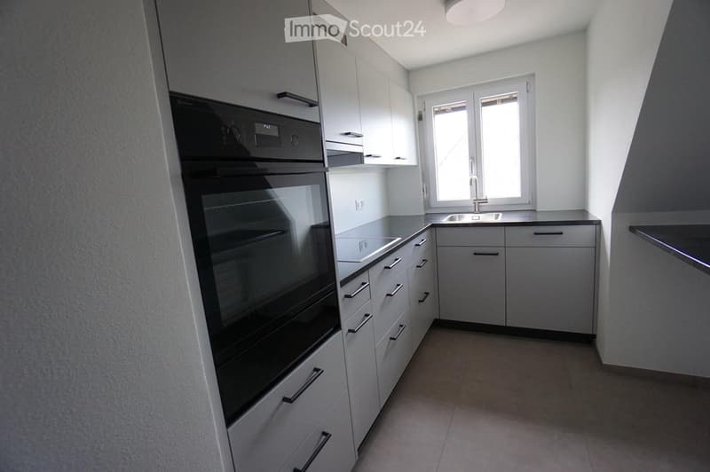 Modern kitchen with white cabinets, stainless steel oven, and a window above the sink.