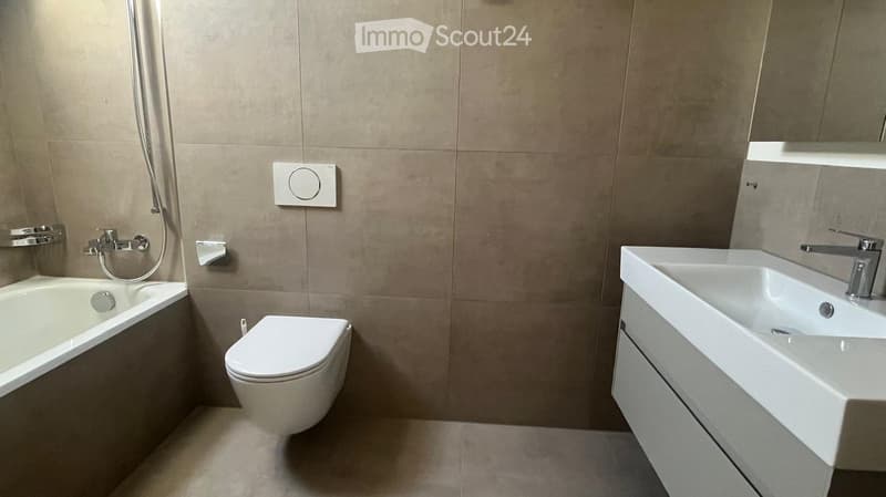 Modern bathroom with a bathtub, toilet, and sink, featuring beige tiles and a sleek design.