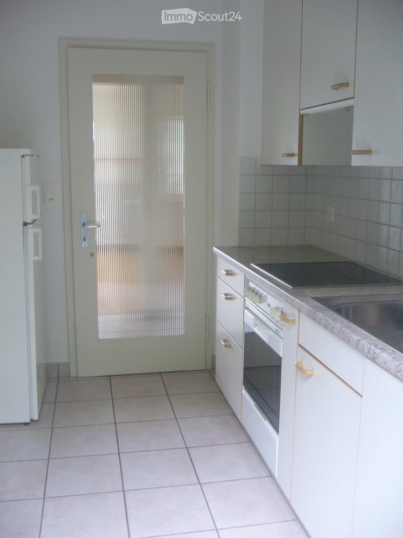 Empty kitchen with white cabinets, tiled floor, and a refrigerator on the left side.