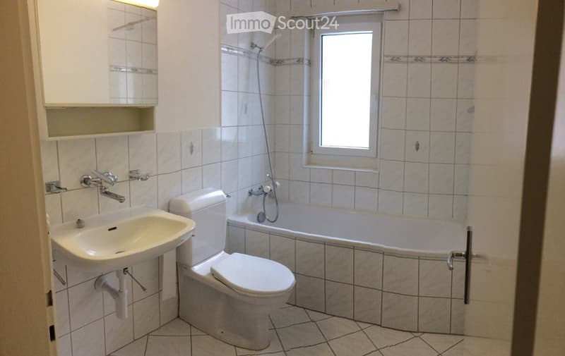 Bathroom with white tiles, a sink, toilet, bathtub, and a window above the bathtub.