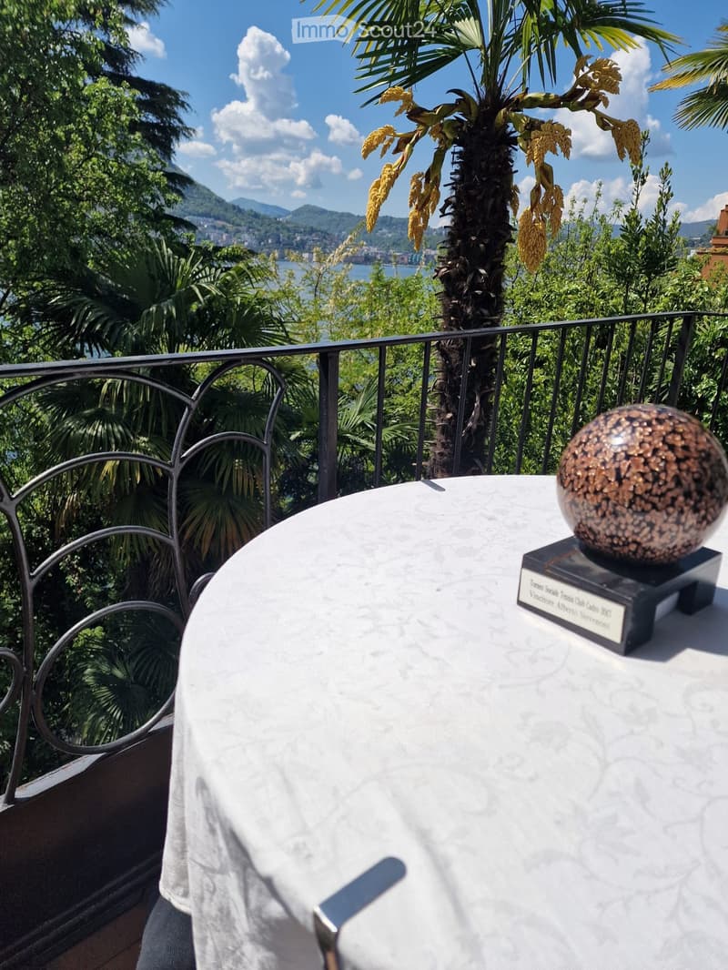 Balcony with a round marble table, a decorative sphere, and a scenic view of a lake and mountains.