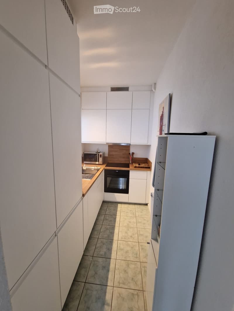Modern kitchen with white cabinets, stainless steel appliances, and a wooden countertop.