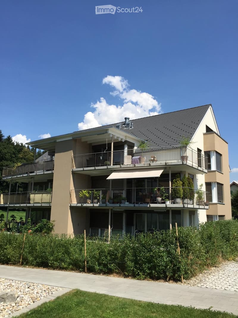 House. Modern two-story house with beige and white exterior, multiple balconies, large windows, and surrounding greenery.