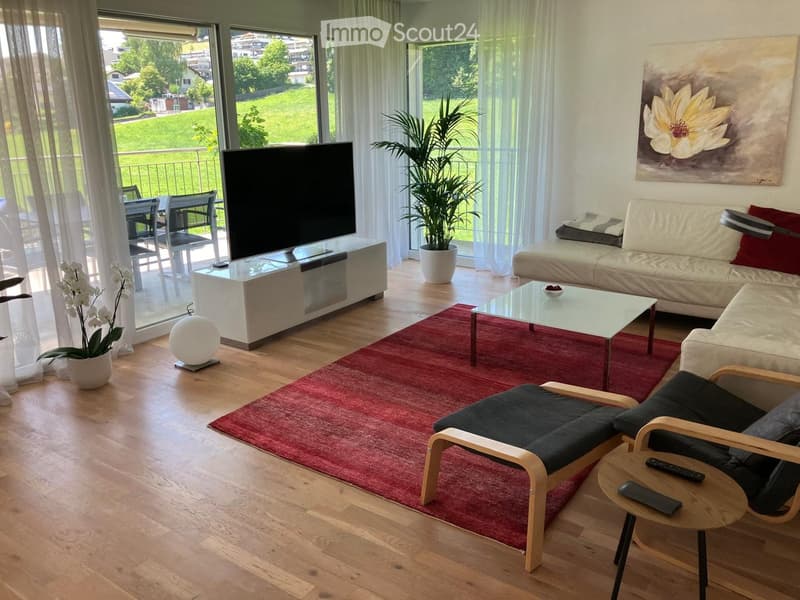 Modern living room with a large window offering a view, a white sofa, a glass coffee table, a TV stand, a round ball lamp, and potted plants.