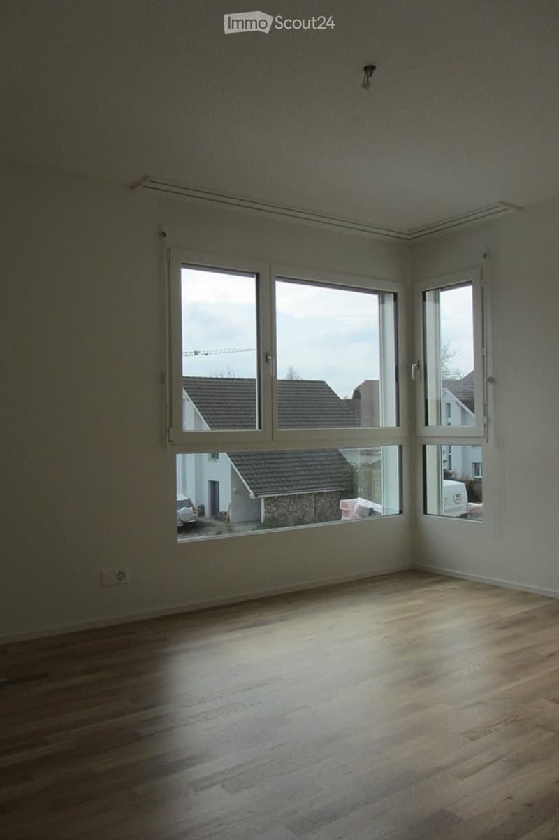 Unfurnished Room. Empty room with wooden flooring and large windows offering a view of neighboring houses and a parked car.