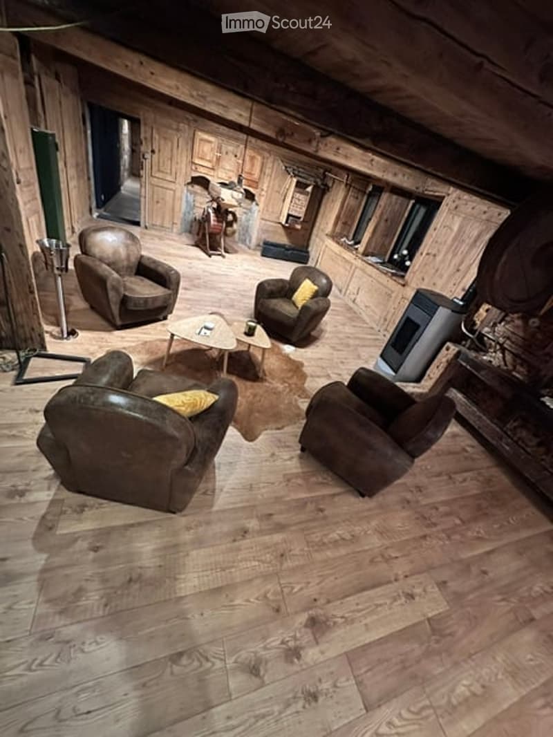 Cozy living room with exposed wooden beams, leather armchairs, coffee table, and warm lighting.