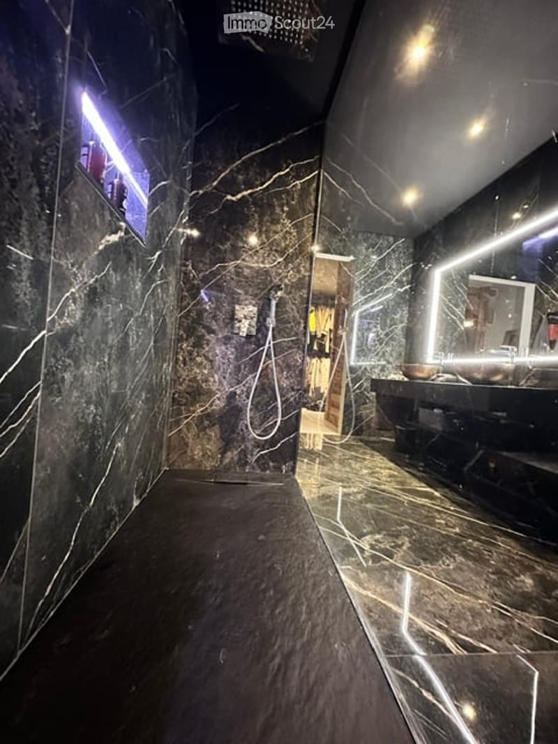 Modern bathroom with dark marble walls and floor, illuminated vanity area, large mirror, and a separate shower area.