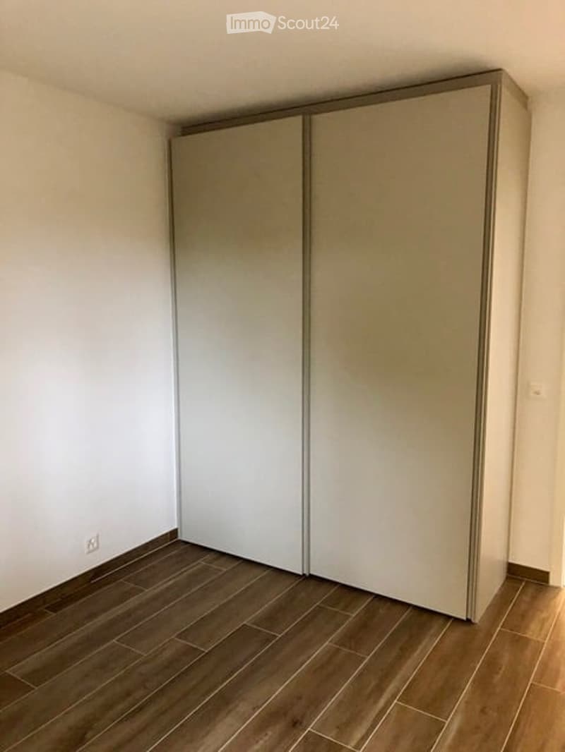 Empty room with wooden flooring and a large, modern sliding wardrobe unit against one wall.