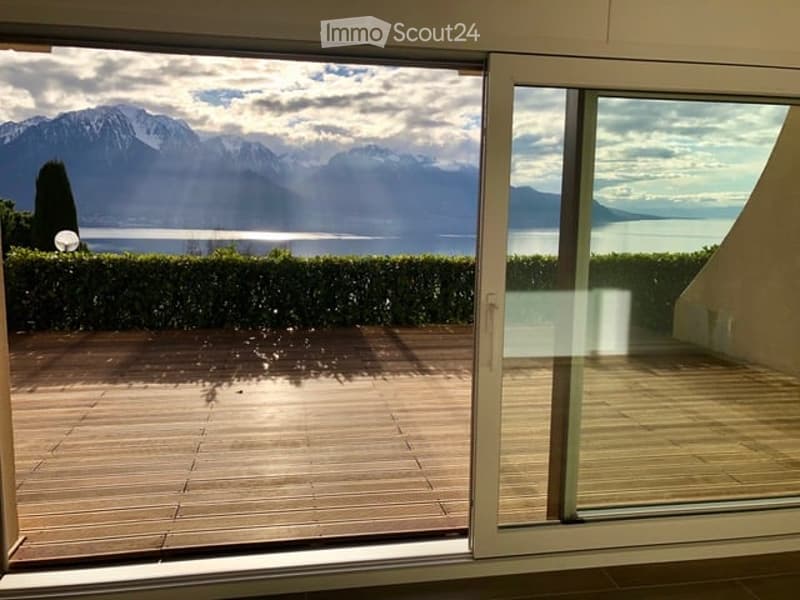 Balcony with wooden decking, large glass sliding doors, scenic mountain and lake view.