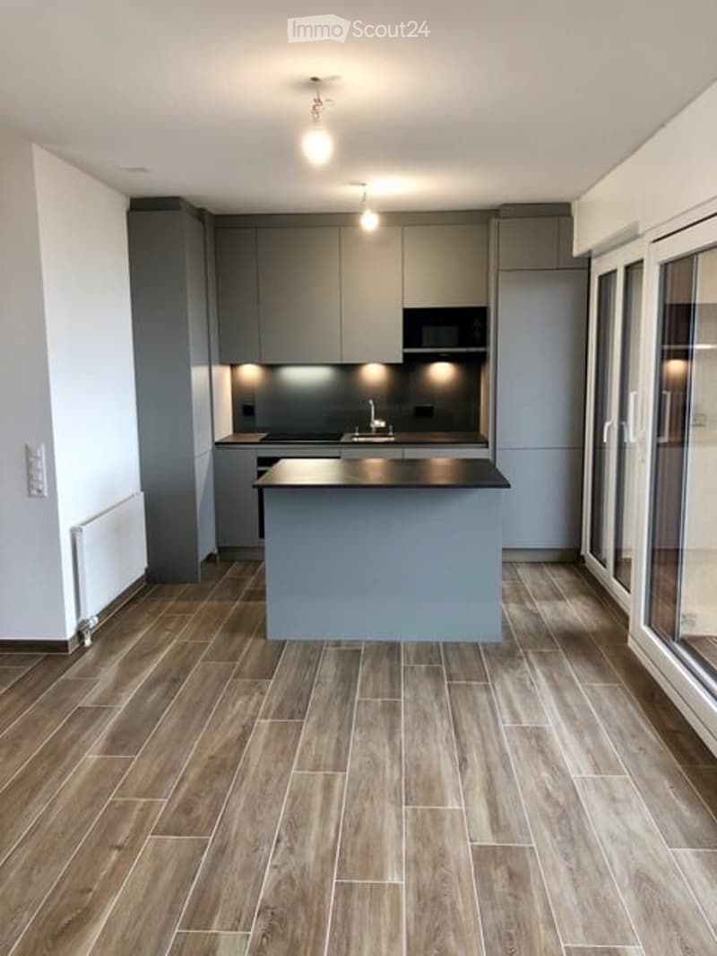Modern kitchen with grey cabinetry, a central island, and wooden flooring. Features include a sink with a modern faucet and built-in lighting.