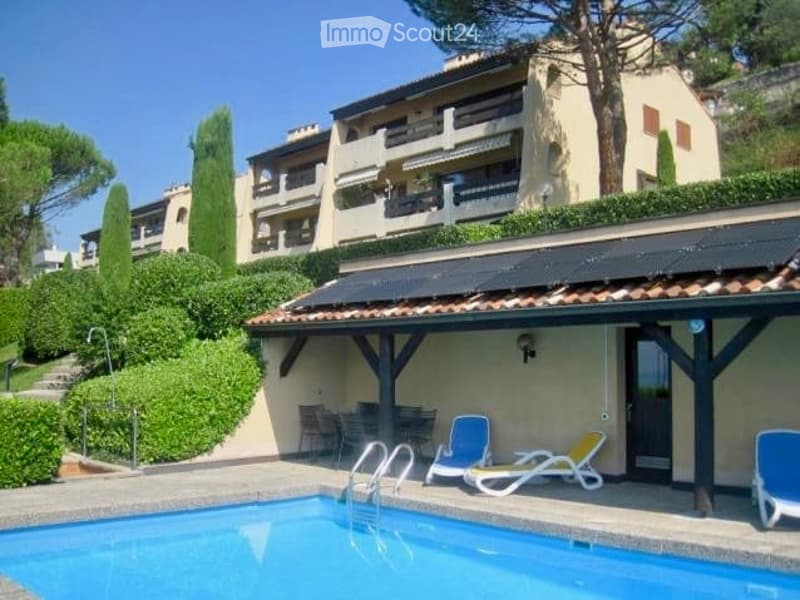 Outdoor area with a swimming pool, lounge chairs, and a covered patio area near a multi-story building.