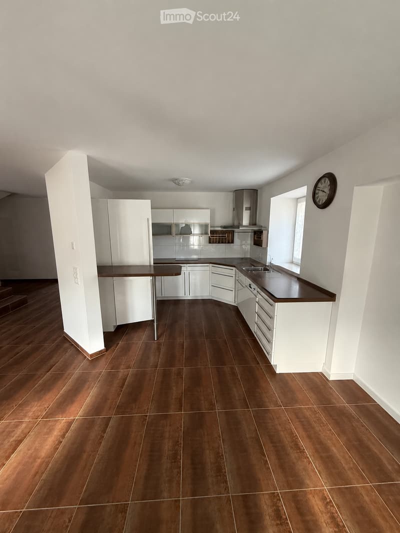 Modern kitchen with white cabinets, dark wooden countertops, and a central island table. The floor is made of dark wood tiles, and there is a window on the right side.