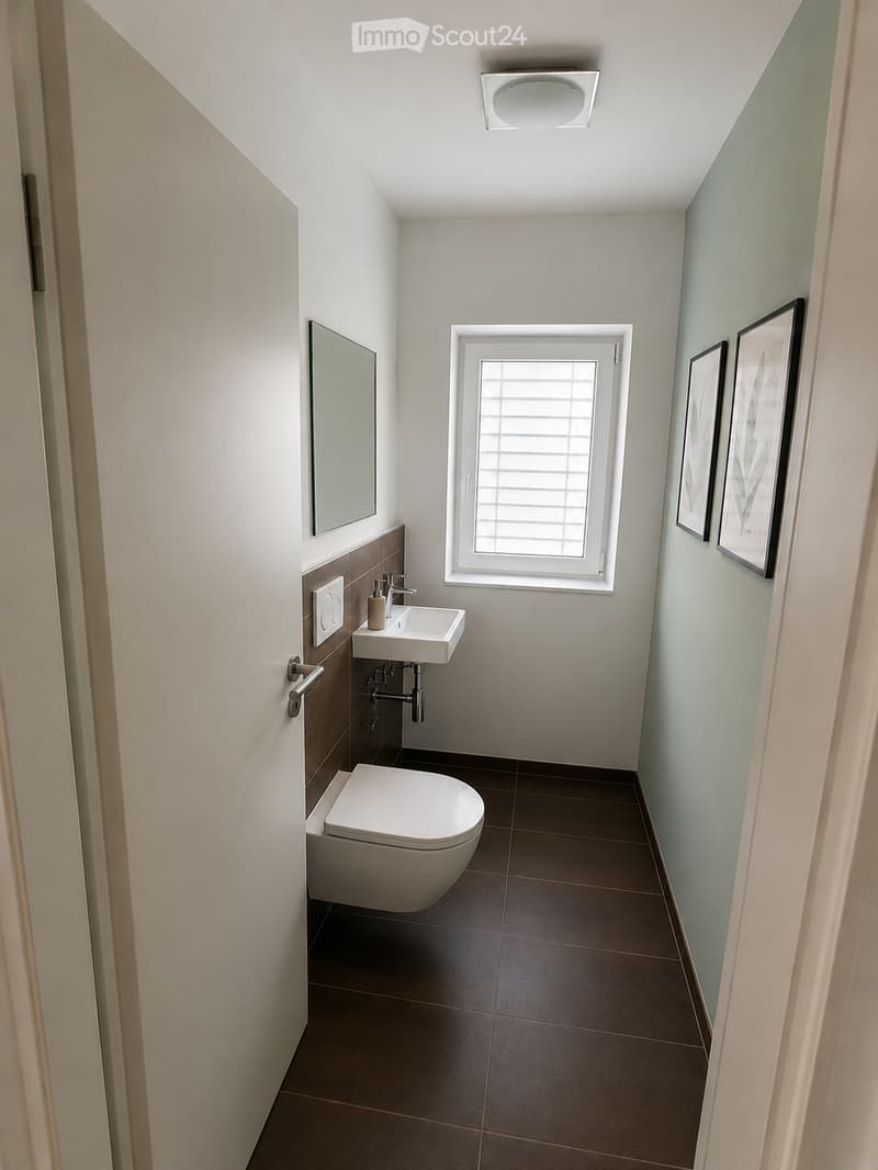 Modern bathroom with a toilet, sink, mirror, and framed picture on the wall. The room features a window with blinds and a sleek, contemporary design.
