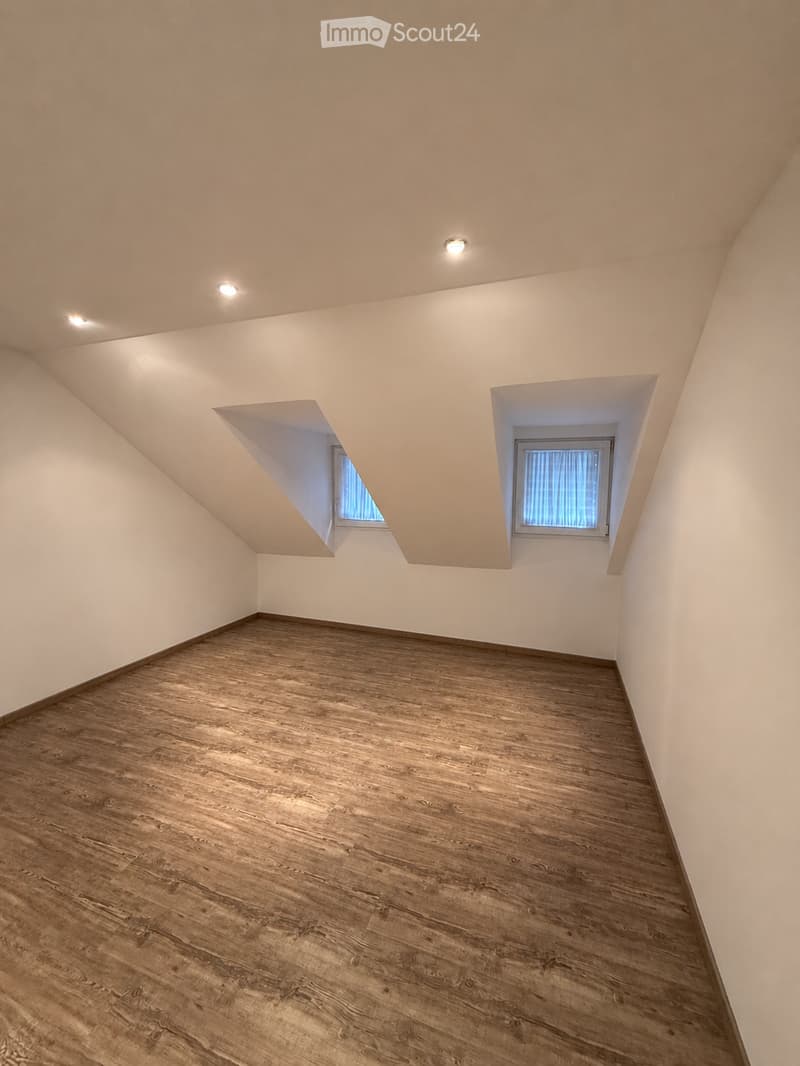 Empty room with wooden flooring and white walls, featuring two small windows and recessed ceiling lights.