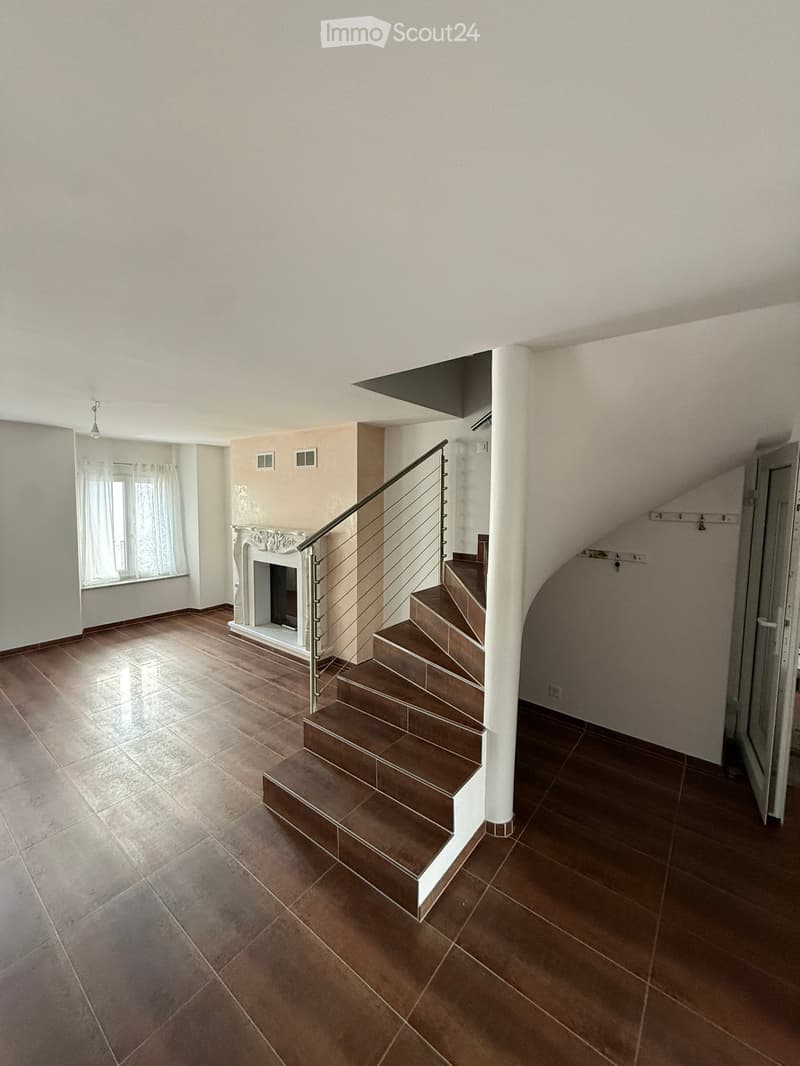 Spacious hallway with a staircase leading upwards, tiled floor, fireplace, and large window with curtains.