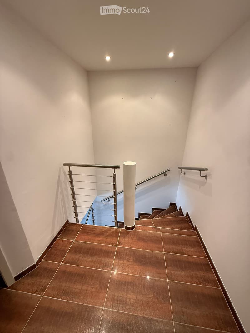 Modern staircase with brown tiled steps, white walls, and stainless steel railings.