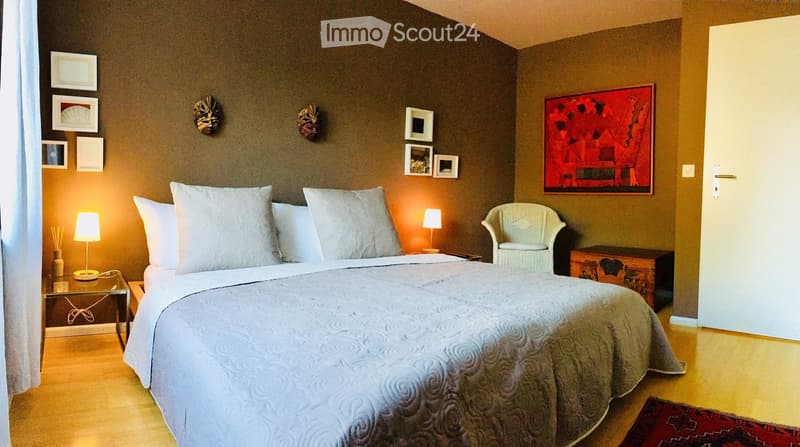 Cozy bedroom with a large bed, nightstands with lamps, a small armchair, and decorative wall art.