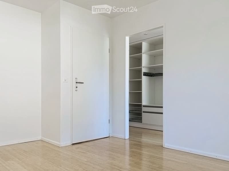Empty room with white walls, wooden floor, and an open closet with empty shelves and drawers.