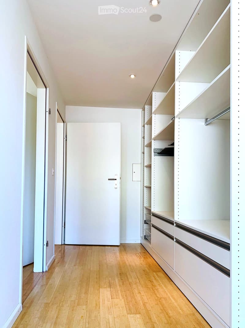 Empty hallway with wooden flooring, white walls, built-in closet with shelves and drawers, and two doors.