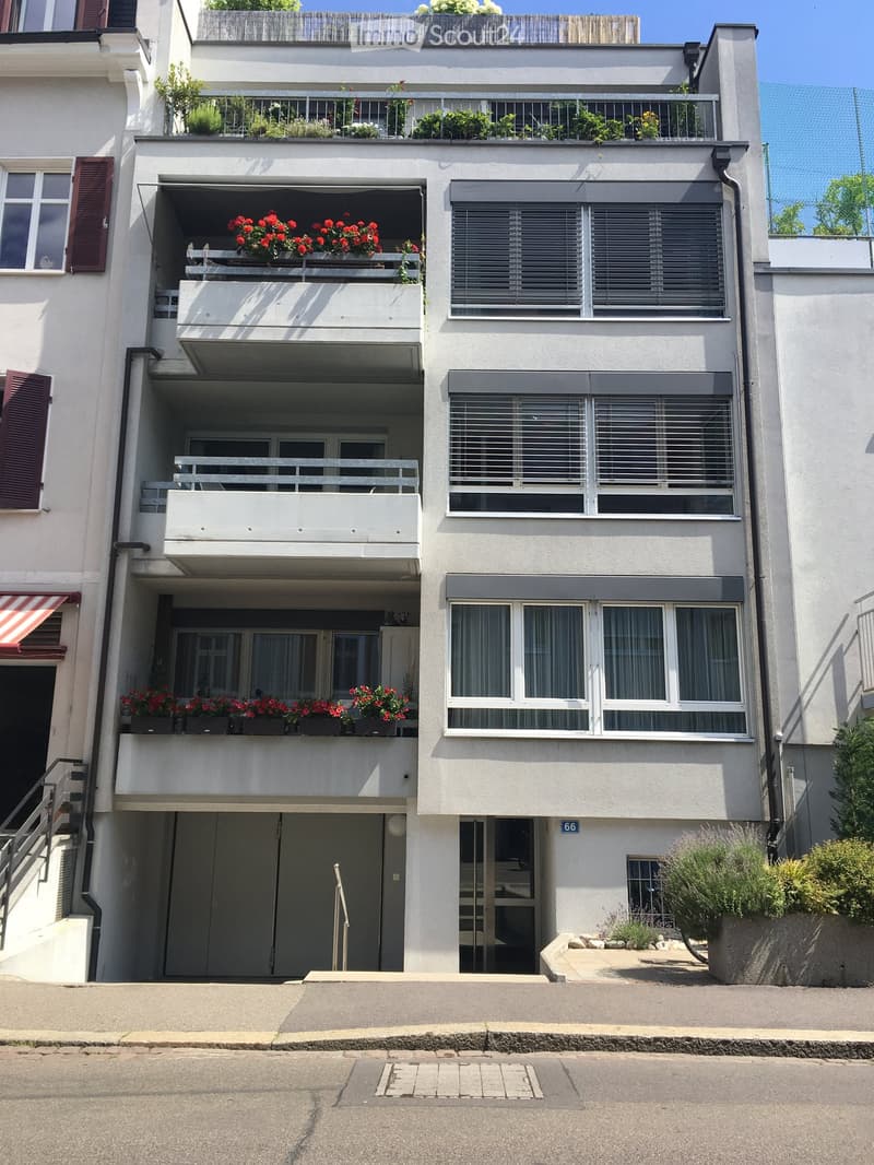 Four-story residential building with balconies, large windows, and flower boxes. Features include a garage entrance, raised ground floor, and decorative shutters.