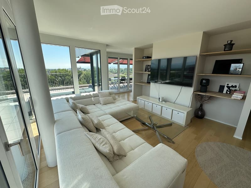 Modern living room with a large sectional sofa, glass coffee table, TV on a shelf, and access to a balcony.