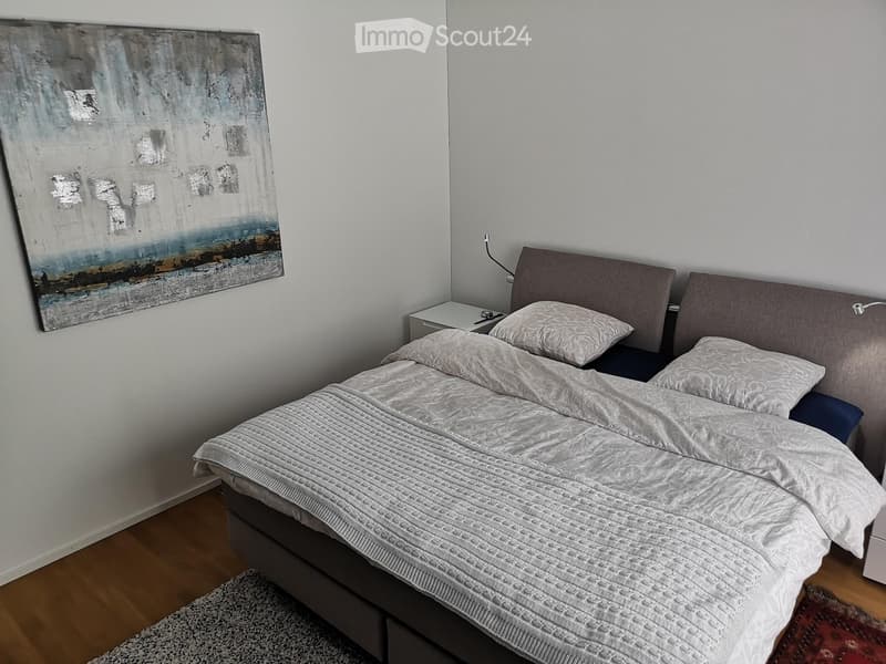 Modern bedroom with a large bed, nightstand, and abstract painting on the wall.