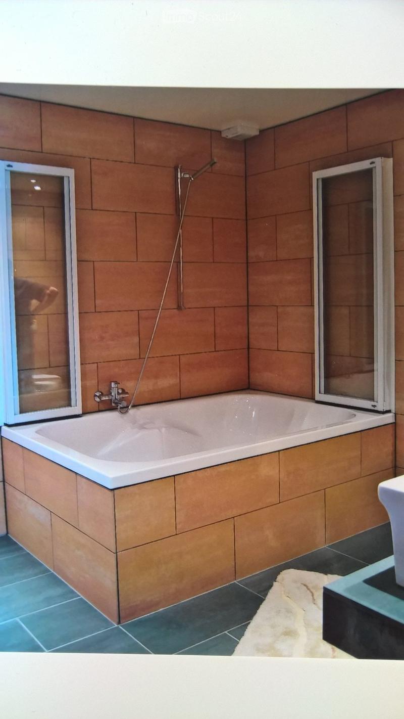 Bathroom with a bathtub, showerhead, and sink. The walls are tiled in a warm brown color, and the floor has blue and dark tiles.