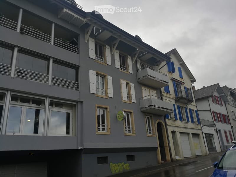 Multi-story residential building with grey facade, white shutters, balconies, and a sign reading "Seniors' Home".