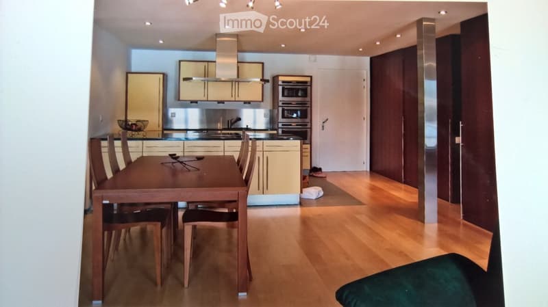 Modern kitchen and dining area with light wood flooring, stainless steel appliances, and a wooden dining table with chairs.