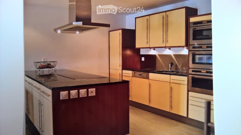 Modern kitchen with light wood cabinets, stainless steel appliances, and a dark countertop island.