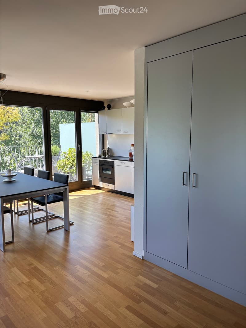 Modern dining area with a sleek black dining table and chairs, adjacent to a contemporary kitchen with white cabinets and stainless steel appliances.