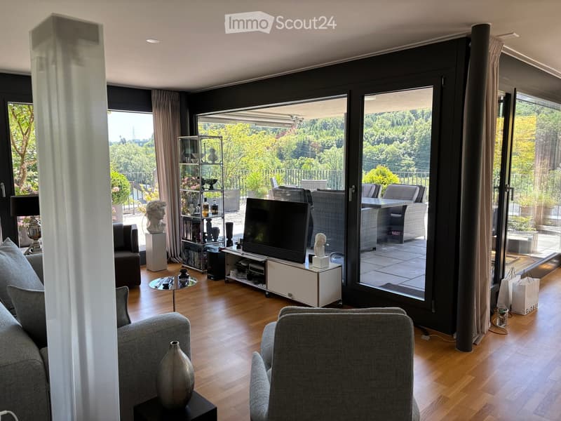 Modern living room with large windows offering a scenic view, featuring a grey sofa, coffee table, television, decorative shelf, and vases.