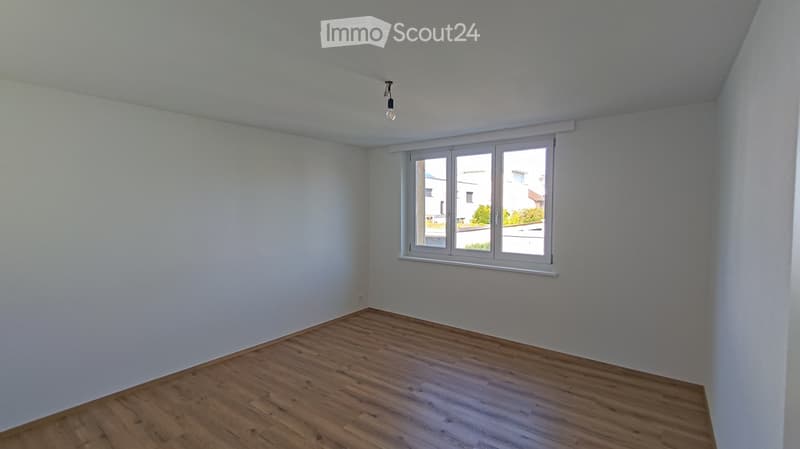 Empty room with light-colored walls, wooden flooring, and a single window with white frame and blinds.