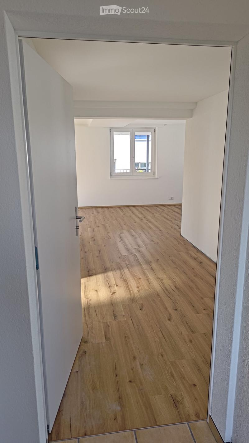 Empty hallway with wooden flooring, white walls, and a window at the end.