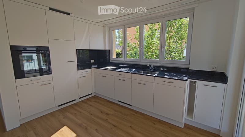 Modern kitchen with white cabinets, black countertops, and a wooden floor. Features an oven, sink, and faucet.
