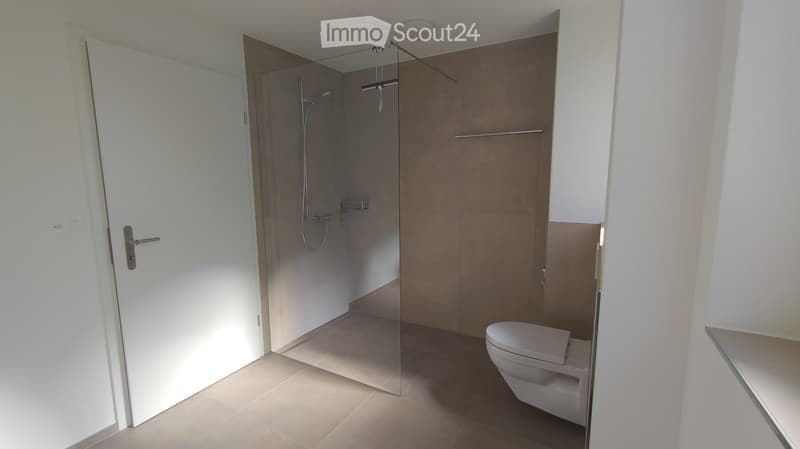Modern bathroom with a glass-enclosed shower, a toilet, and tiled flooring.