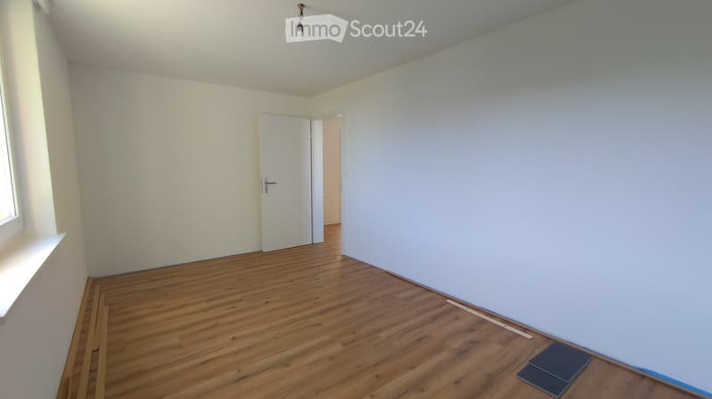 Empty room with wooden flooring, white walls, and a single door leading to another space. No furniture or equipment is present.