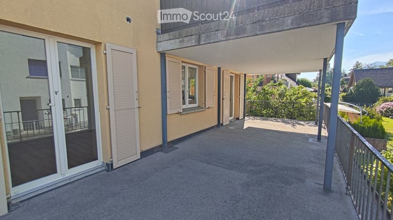 Balcony with concrete floor, metal railing, sliding glass doors, and a view of a garden and neighboring houses.