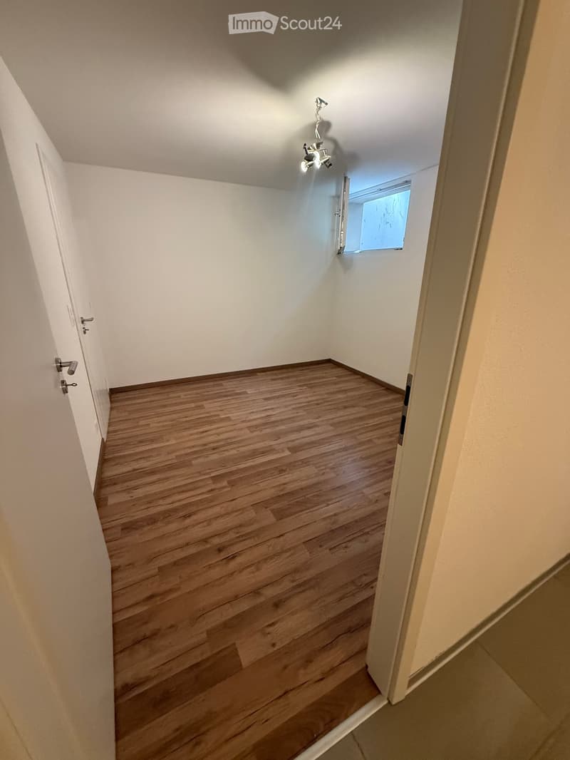 Empty hallway with wooden flooring, white walls, and a small window at the end.