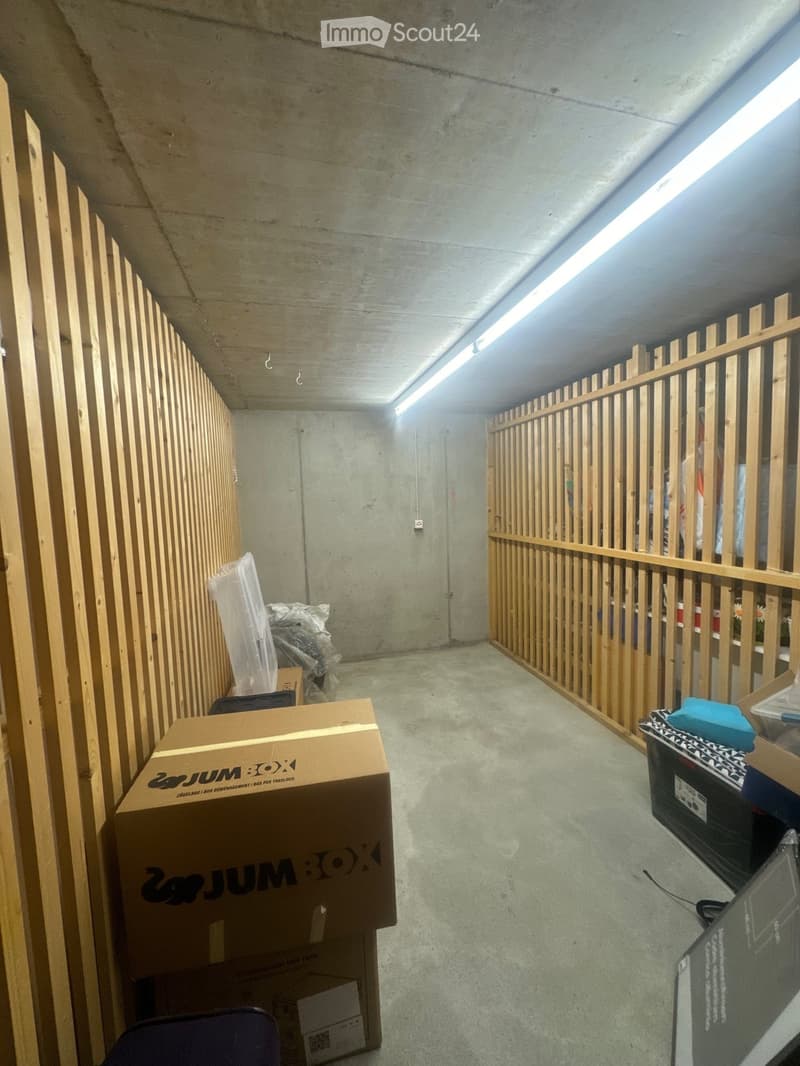 Empty room with concrete walls and floor, wooden paneling on one side, and scattered boxes and items.