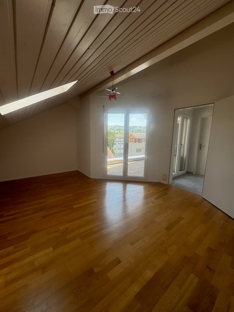 Empty attic room with wooden flooring, white walls, skylight windows, and sliding glass doors leading to a balcony.