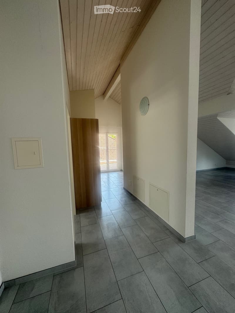 Empty hallway with tiled floor, white walls, and wooden door leading to another room.