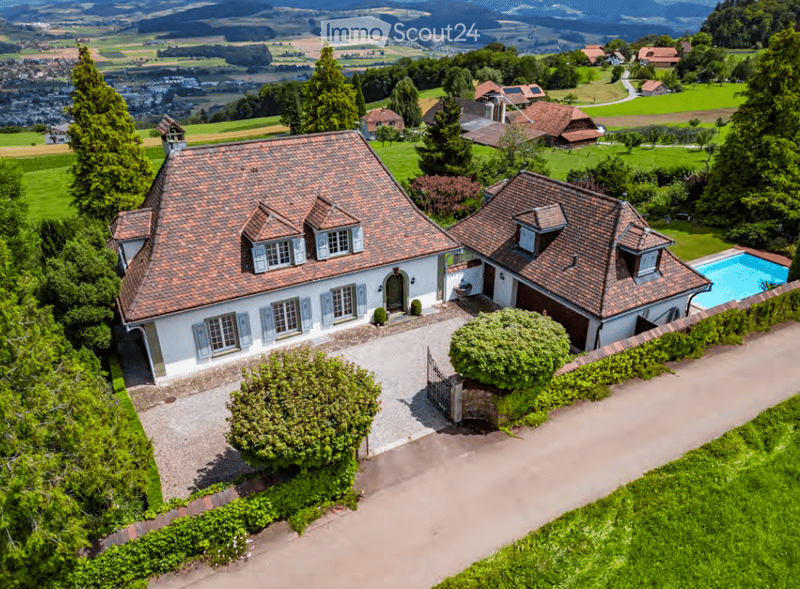 Aerial view of a two-story house with a red-tiled roof, white exterior, and a swimming pool in the garden.